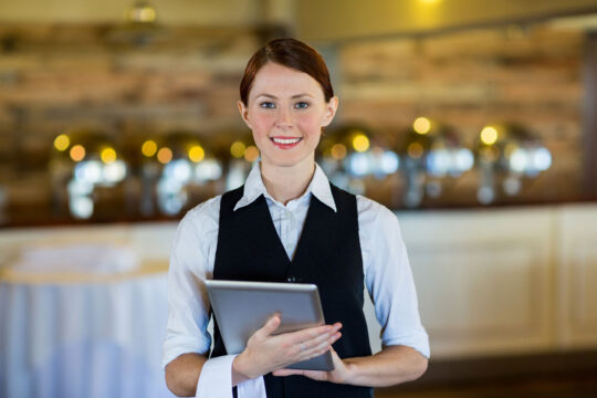 Cameriera che accoglie l'ospite con un tablet per servizio Food & Beverage