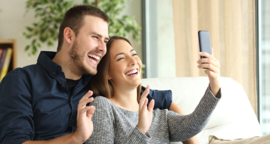 Due ospiti sorridono davanti ad uno smartphone.