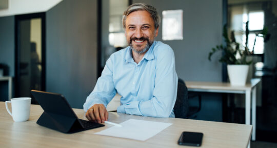 cover blog report finanziario - uomo sorridente alla scrivania con fogli e portatile aperto