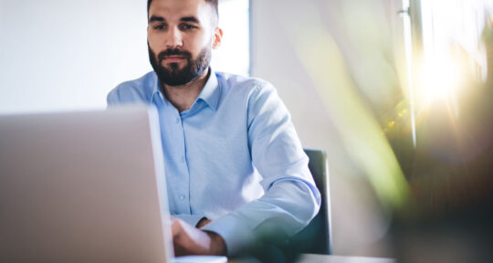 Software CPQ uomo in camicia seduto che digita al portatile